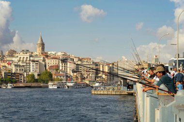 İstanbul, Türkiye - 30 Ağustos 2022: Eminonu İlçesi 'ndeki Galata Kulesi de dahil olmak üzere arka planda İstanbul' un Skyline 'ı ile gün batımından önce Galata Köprüsü' ndeki Golden Horn 'da balık tutan yerel halk