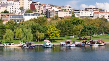 İstanbul, Türkiye - 1 Eylül 2022: Güneşli bir yaz gününde, yoğun büyük ağaçlar ve konut evleri olan yeşil parkın arka planında, Haliç 'in kıyılarına yanaşan tekneler