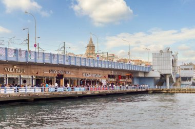 Istanbul, Turkey - August 30, 2022: Galata Bridge with traditional fish restaurants in the passage under the bridge, and crowds of People during Victory Day holiday with Galata Tower in the far end