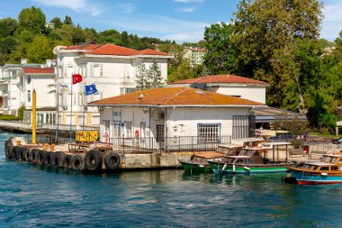 Kanlica İskelesi, veya Kanlica Feribot Terminali, yoğun yeşil ağaçların, beyaz ahşap binaların ve açık gökyüzünün arka planına sahip, İstanbul, İstanbul 'daki İstanbul Boğazı' nın Asya tarafında bir yaz günü,
