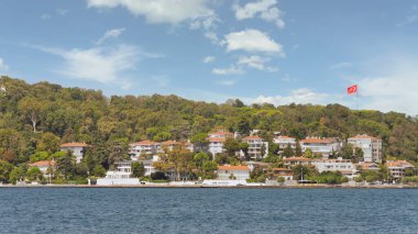 İstanbul Boğazı 'nın Asyalı tarafındaki yeşil dağların denizinden bir yaz günü geleneksel evler ve sık ağaçlarla manzarayı izleyin.