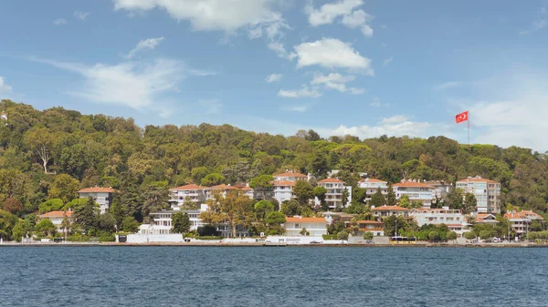 İstanbul Boğazı 'nın Asyalı tarafındaki yeşil dağların denizinden bir yaz günü geleneksel evler ve sık ağaçlarla manzarayı izleyin.