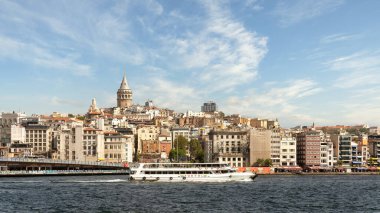 Istanbul, Turkey - August 29 2022: Ferry boat sailing in Bosphorus Strait, with Istanbul skyline in the background, overlooking Galata Bridge with traditional fish restaurants and Galata Tower