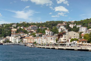 Istanbul, Turkey - August 29, 2022: Arnavutkoy, View from the sea of the green mountains of the Europian side of Bosphorus strait, with docked boats, traditional houses and dense trees in a summer day