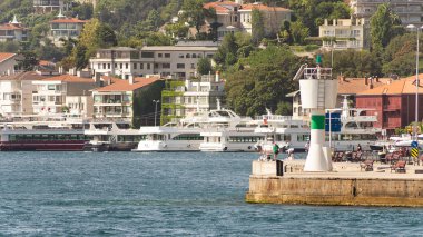 İstanbul, Türkiye - 29 Ağustos 2022: İstanbul Boğazı 'nın Avrupa yakasındaki yeşil dağların denize bakan manzarası, limanlı tekneler, geleneksel evler ve yoğun ağaçlarla dolu bir yaz günü