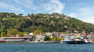 İstanbul, Türkiye ve İstanbul 'da yaz günlerinde limanlı tekneler, geleneksel evler ve sık ağaçlarla, İstanbul Boğazı' nın Avrupa yakasındaki yeşil dağların manzarasına bakın.
