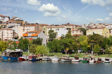 İstanbul, Türkiye - 1 Eylül 2022: Güneşli bir yaz gününde, yoğun büyük ağaçlar ve konut evleri olan yeşil parkın arka planında, Haliç 'in kıyılarına yanaşan tekneler