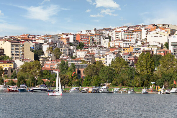 Boats docked at the coast of the Golden Horn, with background of green park with dense big trees, and residential houses, in a sunny summer day, Istanbul, Turkey