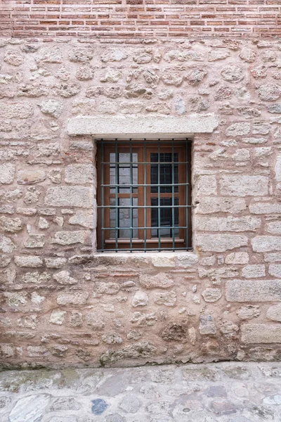在风吹日晒的石墙中 用锻铁棒把窗户关上 这个窗框是用旧木做的 — 图库照片