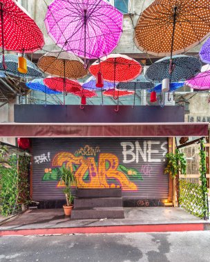 İstanbul, Türkiye - 13 Mayıs 2023: Karaköy Mahallesi 'nde dar bir sokakta renkli grafiti ile kapalı bir dükkan kapısının üzerinde asılı renkli şemsiyeler grubu