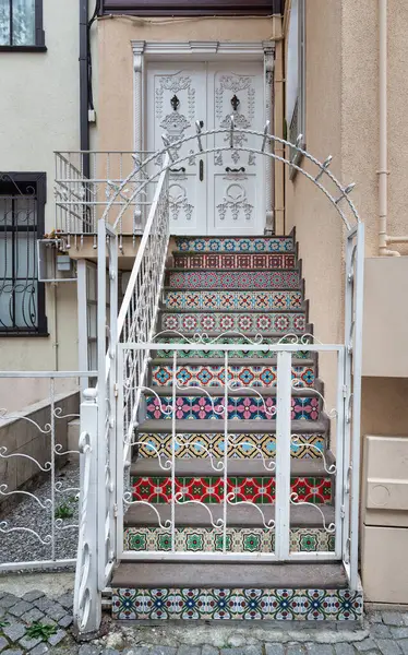 Set of colorful ceramic tiled stairs leading up to a white door decorated with carved inscriptions in Kuzguncuk district, Istanbul, Turkey. The stairs are decorated with various vibrant colors