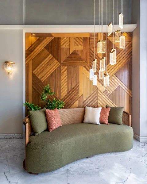 stock image A stylish modern green couch sits in a modern living room with a warm decorated wood cladding wall and a chandelier hanging from the ceiling. The room is decorated with plants and tasteful accessories