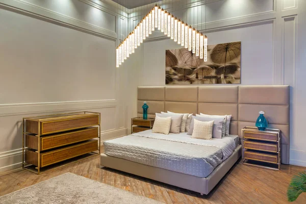 Bedroom with tufted headboard bed, dresser, and nightstands. The bed is made with white bedding. The dresser and nightstands are made of wood with light brown finish. There are lamps on nightstands