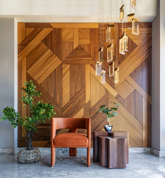 stock image Simple and elegant shot of a modern style orange chair and coffe table in front of a decorated wood cladding wall, with hanging lights and a potted plants