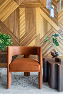 Modern tasarım turuncu bir sandalye ve dekore edilmiş ahşap kaplama bir duvarın önünde asılı ışıklar ve saksı bitkisi olan kahve masasının basit ve zarif görüntüsü.