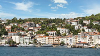 Istanbul, Turkey - August 29, 2022: Arnavutkoy, View from the sea of the green mountains of the Europian side of Bosphorus strait, with docked boats, traditional houses and dense trees in a summer day
