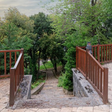 Zengin yeşilliklerle çevrili taş merdiven sakin bir bahçeye iniyor ve alacakaranlıktaki bir parkın huzurlu özünü yakalıyor.