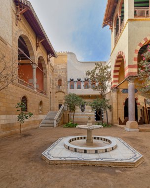 Serene courtyard showcases the timeless beauty of Mamluk architecture with high big arches and stonework with welcoming staircase leading to ornate balcony. A classic marble fountain sits at center clipart