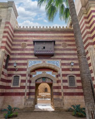Striking red and white striped arched entrance leads into a Mamluk era style building, showcasing intricate architectural details surrounded by lush palm trees clipart