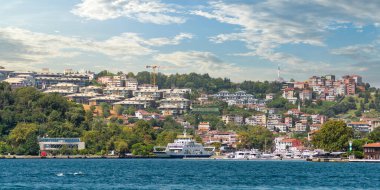 İstanbul Boğazı 'nın Asyalı tarafındaki yeşil dağların denizinden bir yaz günü geleneksel evler ve sık ağaçlarla manzarayı izleyin.