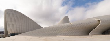 Azerbaycan 'ın Bakü kentindeki ikonik Heydar Aliyev Merkezi, bulutlu bir gökyüzüne karşı çağdaş mimariyi akıcı, dalga benzeri tasarımıyla sergiliyor. Bina Mimar Zaha Hadid tarafından tasarlandı. 