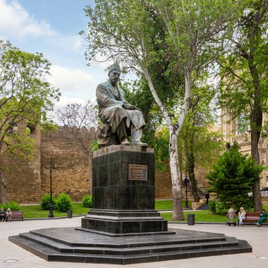 Baku, Azerbaijan - May 5, 2024: Bronze statue of Mirza Alakbar Sabir, a prominent Azerbaijani poet, sits in Sabir Garden. Behind the statue is the Old City stone wall, and lush greenery clipart