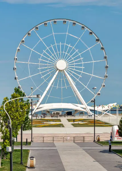 stock image Baku, Azerbaijan - May 4, 2024: A view of the Baku Eye Ferris Wheel, located beside Deniz Mall. The wheel is in the background with few people walking in the foreground.