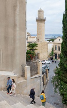 Baku, Azerbaijan - May 5, 2024: Visitors walk down the stairs in the Old City, Icherisheher, with the minaret of the historic Beyler Mosque and charming streets visible clipart