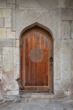 Çok güzel detaylandırılmış ahşap bir kapı tarihi mimari sergilenen yıpranmış taş bir duvara işlenmiş süslü oymalar içerir.