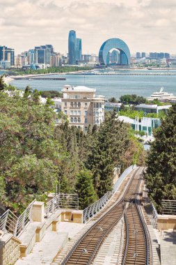Bakü, Azerbaycan manzarası. Ön planda, Bakü Funicular demiryolu yemyeşil bir alandan geçiyor. - Arka planda, şehir silueti Hazar Denizi boyunca uzanıyor.