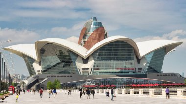 Bakü, Azerbaycan - 4 Mayıs 2024: Ziyaretçiler, güneşli bir günde eşsiz mimari ve canlı atmosferin keyfini çıkararak Deniz Mall yakınlarındaki yürüyüş yolu boyunca yürüyorlar