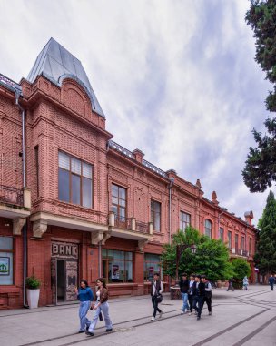 Ganja, Azerbaycan - 13 Mayıs 2024: Ziyaretçiler bulutlu bir gökyüzü altında canlı yeşillik ve eşsiz tuğla mimari ile çevrili Javad Khan Caddesi boyunca sakin bir yürüyüş yapıyorlar