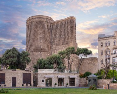 Bakü, Azerbaycan 'daki Meydan Kulesi, akşam gökyüzündeki bulutlara karşı dimdik duruyor. Tarihi binayı saran yemyeşil bir zemin var.