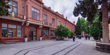 Ganja, Azerbaijan - May 13, 2024: Javad Khan Street, surrounded by vibrant greenery and unique brick architecture under a cloudy sky clipart