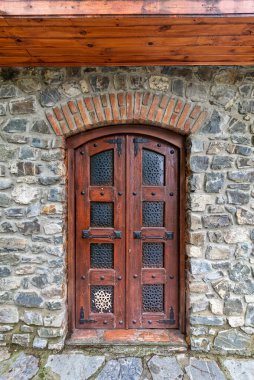 The sturdy wooden door features intricate metalwork, providing a rustic charm, framed by a weathered stone wall in a peaceful rural setting clipart