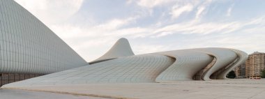 Azerbaycan 'ın Bakü kentindeki ikonik Heydar Aliyev Merkezi, günbatımından önce bulutlu bir gökyüzüne karşı, akışkan, dalga benzeri tasarımı ile modern mimariyi sergiliyor. Mimar Zaha Hadid tarafından tasarlandı.