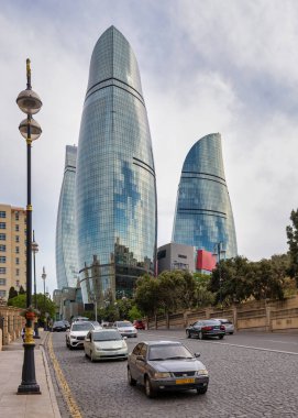 Bakü, Azerbaycan - 6 Mayıs 2024: İkonik Alev Kuleleri, bulutlu bir günde şehrin dinamik enerjisini yansıtan canlı bir Bakü sokak sahnesinin ortasında görkemli bir şekilde yükselir