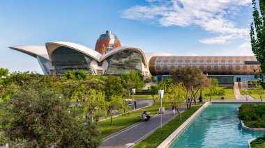 Bakü, Azerbaycan - 4 Mayıs 2024: Ziyaretçiler, yemyeşil alanlar arasında Küçük Venedik 'in pitoresk kanallarını rahatça geçiyorlar. Arka planda Halı Müzesi ve Deniz Alışveriş Merkezi yer alıyor.