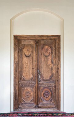 A beautifully crafted wooden door adorned with detailed carvings showcases traditional craftsmanship. Set against a neutral wall, it adds character to the architectural interior clipart