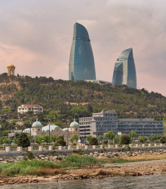 Bakü, Azerbaycan 'da ikonik bir dönüm noktası olan Alev Kuleleri, yemyeşil ve pitoresk kıyı şeridinden zarif bir şekilde yükselen güneş ışığını yakalayan parlak yansımaları ile dimdik ayakta duruyor.