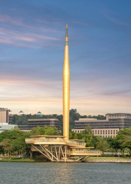 Milenyum Anıtı Alaf Baru renkli günbatımına karşı görkemli bir şekilde ayakta duruyor. Altın ucu gölün sakin sularında yansıyarak Putrajaya, Malezya 'da sakin bir atmosfer yaratıyor.
