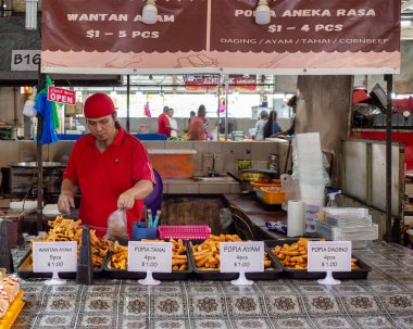 Bandar Seri Begawan, Brunei - 26 Şubat 2025: Gadong Gece Pazarı 'nda kızarmış atıştırmalık paketleyen bir satıcı. Açık tabela reklamları çeşitli Popia ve Wantan seçenekleri
