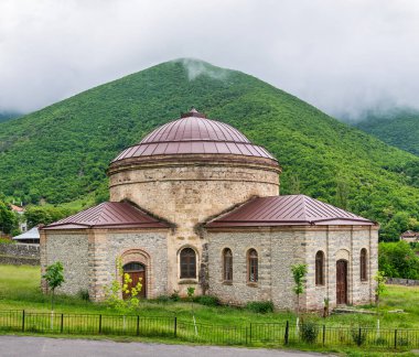 Yuvarlak Tapınak olarak bilinen Üç Azize Kilisesi, Shaki, Azerbaycan 'daki yemyeşil manzaralar ve sis kaplı dağların arasında yer almaktadır.