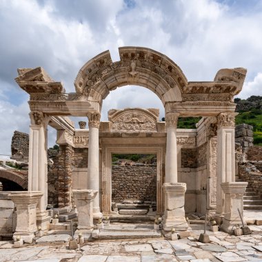 Efes, Seluk, İzmir, Türkiye 'deki Hadrian Tapınağı, tarihi kalıntılarla çevrili karmaşık mimariyi gözler önüne seriyor. Yapı dramatik bir gökyüzüne karşı görkemli bir şekilde duruyor.