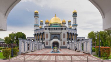 Bandar Seri Begawan, Brunei - 23 Şubat 2025: Bir kemer tarafından çerçevelenmiş Jame Asr Hassanil Bolkiah Camii 'nin çarpıcı mimarisi. Altın kubbe sakin bir gökyüzünün altında parlıyor ve huzurlu bir atmosfer yaratıyor.