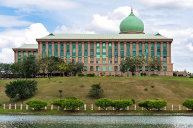 Perdana Putra, başbakanlık ofisi, Putrajaya, Malezya. Yeşil kubbeli, sütunlu ve bulutlu gökyüzünün altında göl manzaralı ikonik hükümet binası.