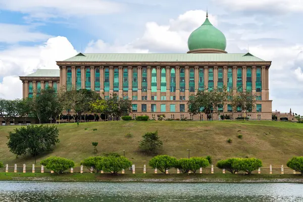 Perdana Putra, başbakanlık ofisi, Putrajaya, Malezya. Yeşil kubbeli, sütunlu ve bulutlu gökyüzünün altında göl manzaralı ikonik hükümet binası.