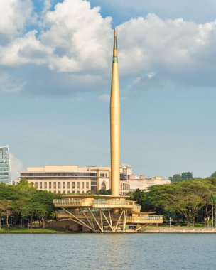 Milenyum Anıtı ya da Malezya 'nın Putrajaya kentindeki göl kıyısında bulunan önemli bir altın tarihi eser olan Monumen Alaf Baru' nun manzarası. Modern mimari, ağaçlar ve bulutlu bir gökyüzü.