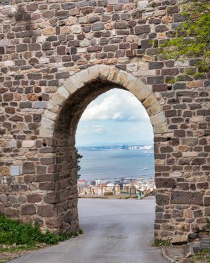 Türkiye 'nin İzmir kentindeki Kadifekale şatosunun antik taş kemer yolu, İzmir Körfezi manzarası ve bulutlu bir gökyüzü altındaki uzak dağlar sunuyor