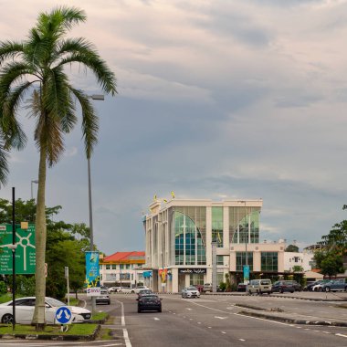 Bandar Seri Begawan, Brunei - 23 Şubat 2025: Melvida binası, palmiye ağaçları ve bulutlu gökyüzü altındaki araçların yer aldığı şehir caddesi